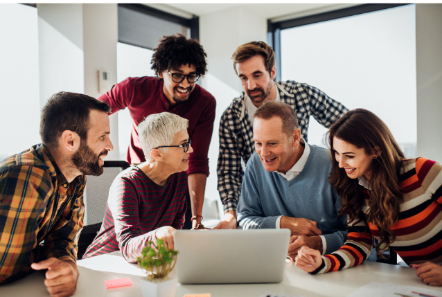 A group of diverse colleagues collaborating around a laptop in a bright, modern office space. Represents teamwork and planning.