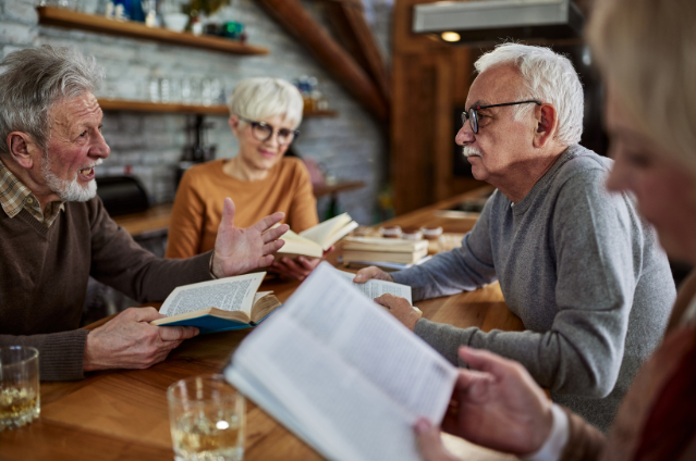 A group of seniors having a lively discussion while reading books, highlighting how book clubs and group learning help keep your mind sharp in retirement.