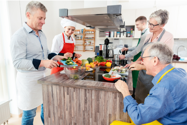 A group of people in a kitchen, preparing meals together with fresh produce and vibrant smiles.