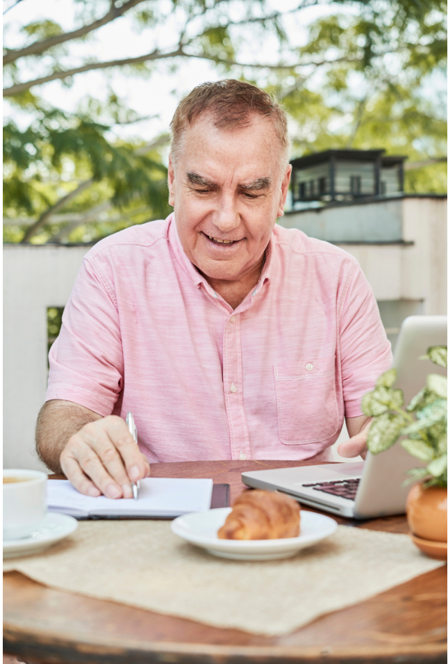 A man working on a laptop and taking notes outdoors, symbolizing focus and consistency to stay on track with retirement goals.