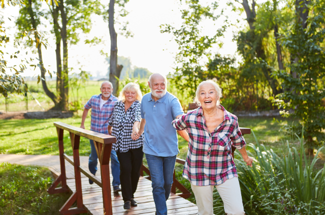 A group of older adults happily walking across a wooden bridge outdoors, highlighting the benefits of physical activity for keeping your mind sharp in retirement.