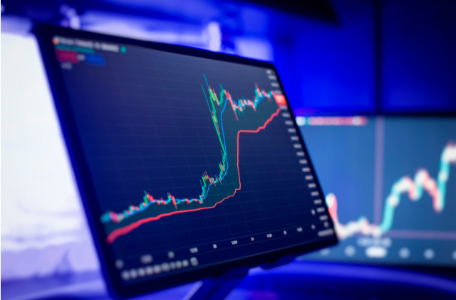 A monitor displaying fluctuating financial charts in a dimly lit room. Illustrates the importance of monitoring investments and finances for a location-independent retirement.