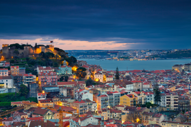 A panoramic view of a picturesque European city at sunset, with a historic castle in the background. Reflects the travel opportunities available in digital nomad retirement.