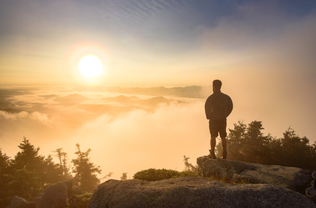 A lone figure standing on a mountain peak, gazing at a glowing sunrise over a mist-filled valley. Represents the sense of freedom and exploration central to a nomadic retirement lifestyle.