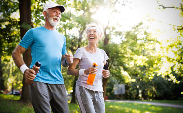 A senior couple jogging outdoors while smiling, illustrating how physical activity helps with keeping your mind sharp in retirement.