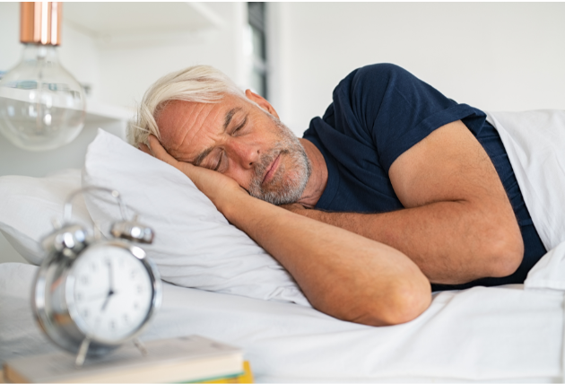 An older man sleeping peacefully in bed with an alarm clock nearby, emphasizing the importance of quality sleep for keeping your mind sharp in retirement.
