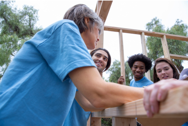 Group of volunteers building a wooden structure together, demonstrating teamwork and community support.