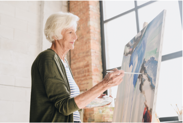 An older woman painting on a canvas in a sunny studio, illustrating creative midday activities for retirees seeking fulfillment and growth.