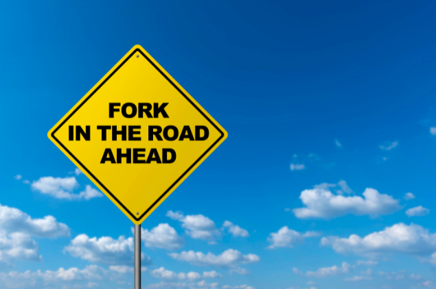 Yellow road sign reading 'Fork in the Road Ahead' against a blue sky, representing decision points in retirement planning.
