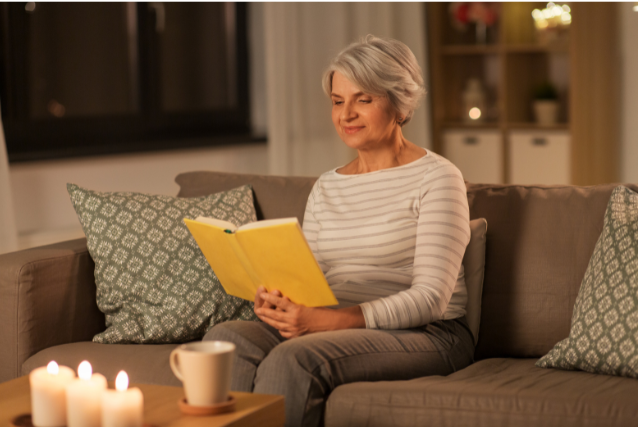 A woman relaxing with a book and a cup of tea by candlelight, reflecting a calming evening routine for how to plan a fulfilling day in retirement.