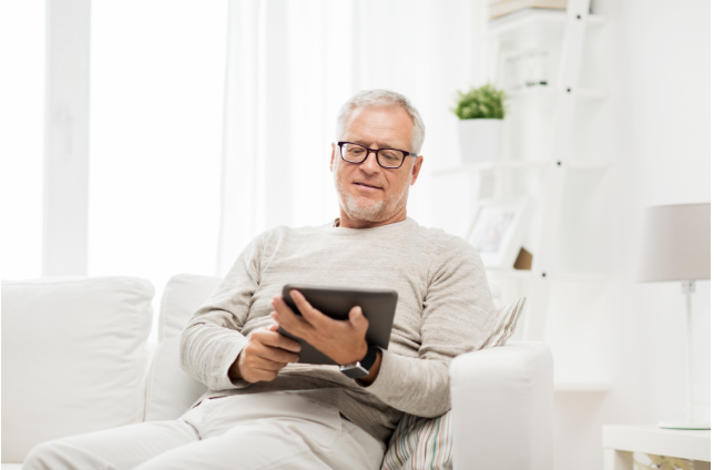 An older man sitting comfortably with a tablet in his hand, showing how staying mentally engaged with technology can contribute to keeping your mind sharp in retirement.