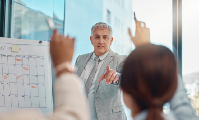 Professional financial planner presenting to an audience, with a calendar on a whiteboard in the background, emphasizing planning strategies.