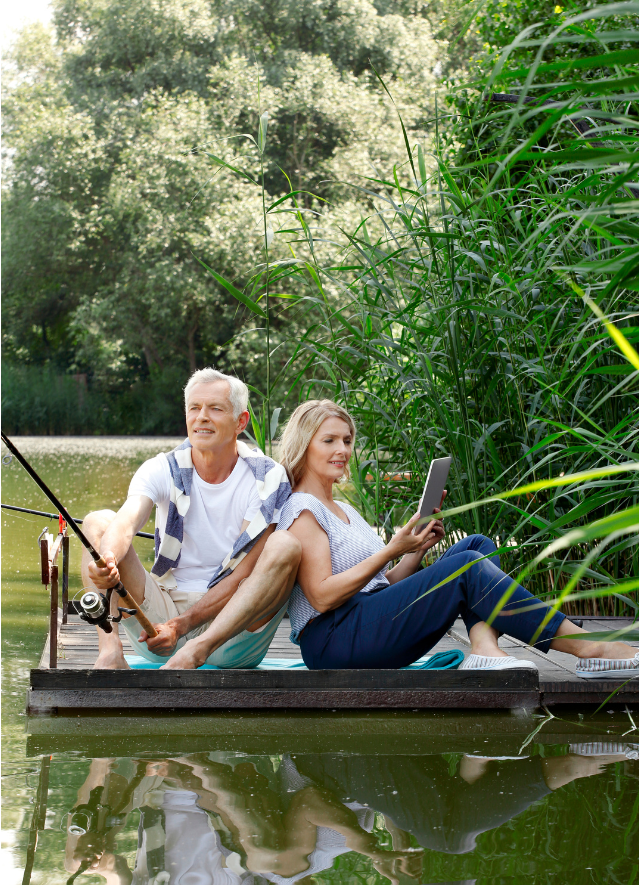 A couple enjoying fishing and reading by a serene lake, illustrating peaceful hobbies that help avoid pitfalls in retirement planning.