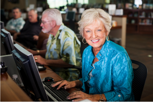 A smiling older woman sitting at a computer in a community center.