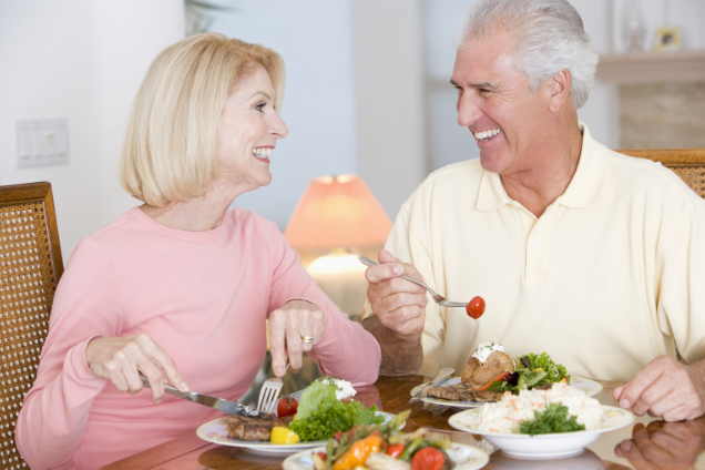 Smiling older couple sharing a healthy meal at home, illustrating that proper nutrition and shared moments are vital for busting myths about aging and well-being.