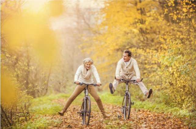 A joyful senior couple riding bicycles on a leaf-covered path during autumn, showcasing active lifestyles that debunk myths about aging and physical limitations.