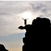 A silhouette of a person standing triumphantly on a mountain peak, representing overcoming the fear of irrelevance after retirement and embracing new opportunities.