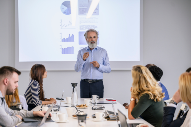 An older professional presenting data in a meeting, highlighting how retirees stay relevant in the workforce and embrace an anti-retirement lifestyle of continued growth and leadership.