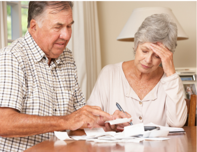 A senior couple at a table reviewing bills and financial statements, highlighting the challenges of financial planning in retirement and the need for alternative income strategies in an anti-retirement lifestyle.