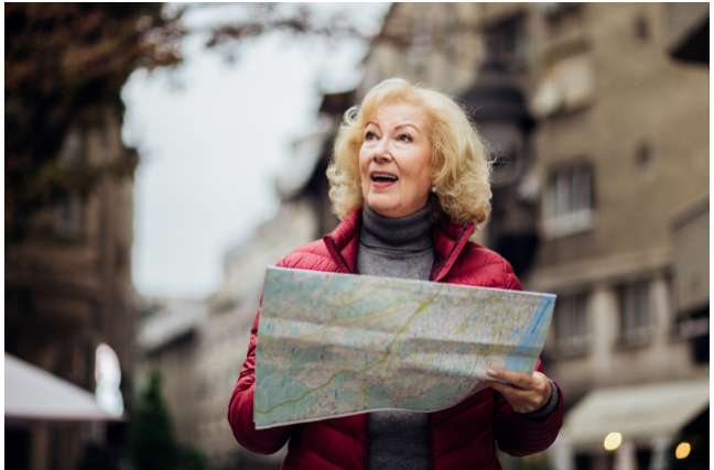 A smiling older woman holding a map while exploring a new city, symbolizing travel, independence, and adventure.