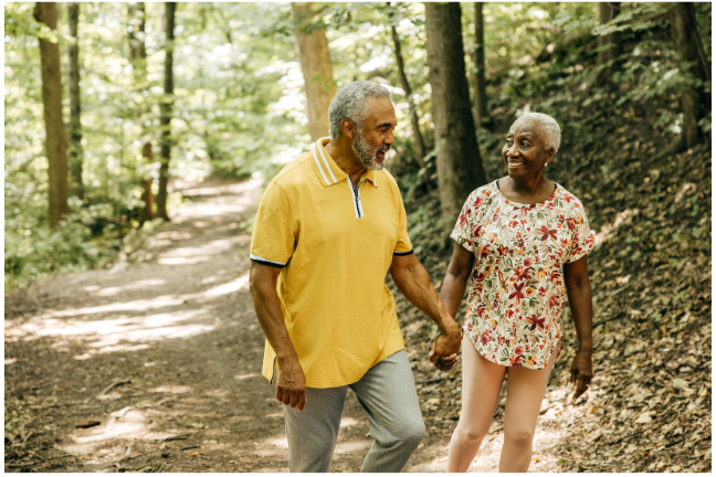 An active senior couple walking hand-in-hand on a forest trail, showcasing the importance of health, movement, and adventure in an anti-retirement lifestyle.