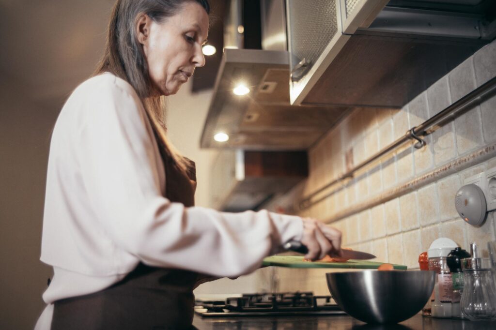 Mature woman cooking in her kitchen, incorporating enjoyable daily activities into retirement routine planning.