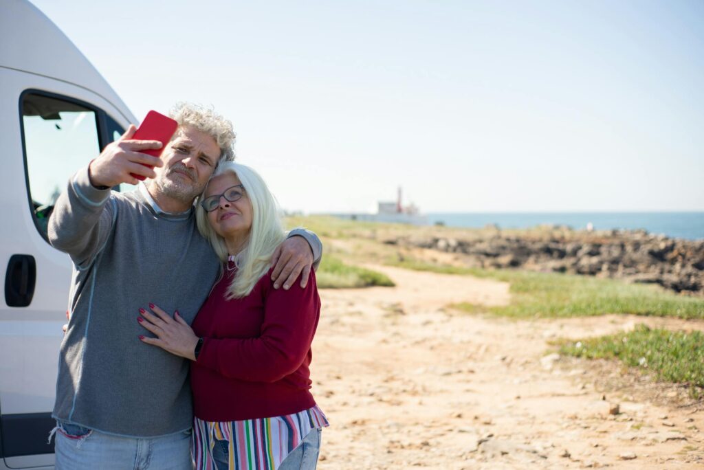 A happy older couple embracing and taking a selfie near their camper van, enjoying the freedom of an anti-retirement lifestyle with travel and adventure.