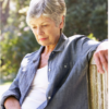 An elderly woman sitting on a wooden park bench, looking down with a contemplative expression—illustrating the emotional impact of loneliness in retirement.