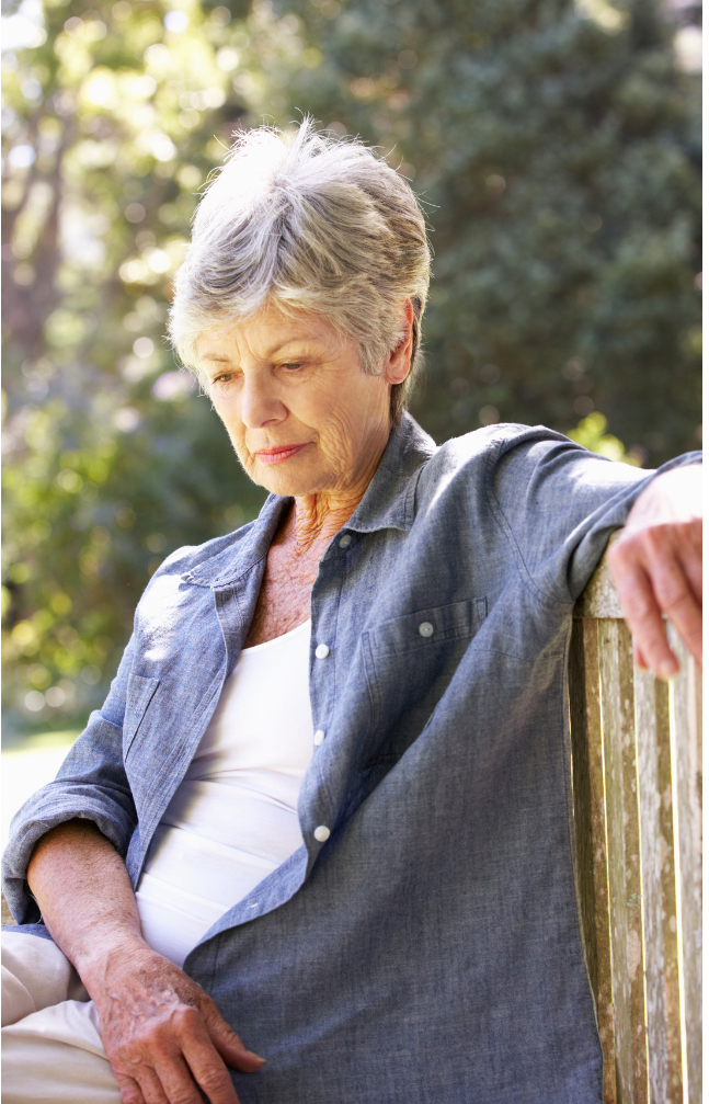 An elderly woman sitting on a wooden park bench, looking down with a contemplative expression—illustrating the emotional impact of loneliness in retirement.