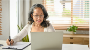 A mature woman working on her laptop from home, representing the flexibility and independence of consulting after 50.