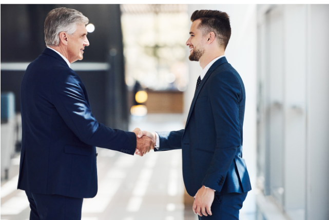 A senior professional shaking hands with a younger client, symbolizing trust, experience, and networking in consulting after 50.