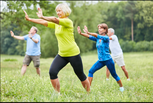A group of older adults practicing Tai Chi in a lush green park.