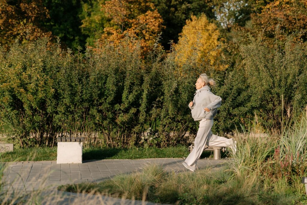 Older woman jogging outdoors in a park, staying active and healthy—one of many energizing things to do in retirement.